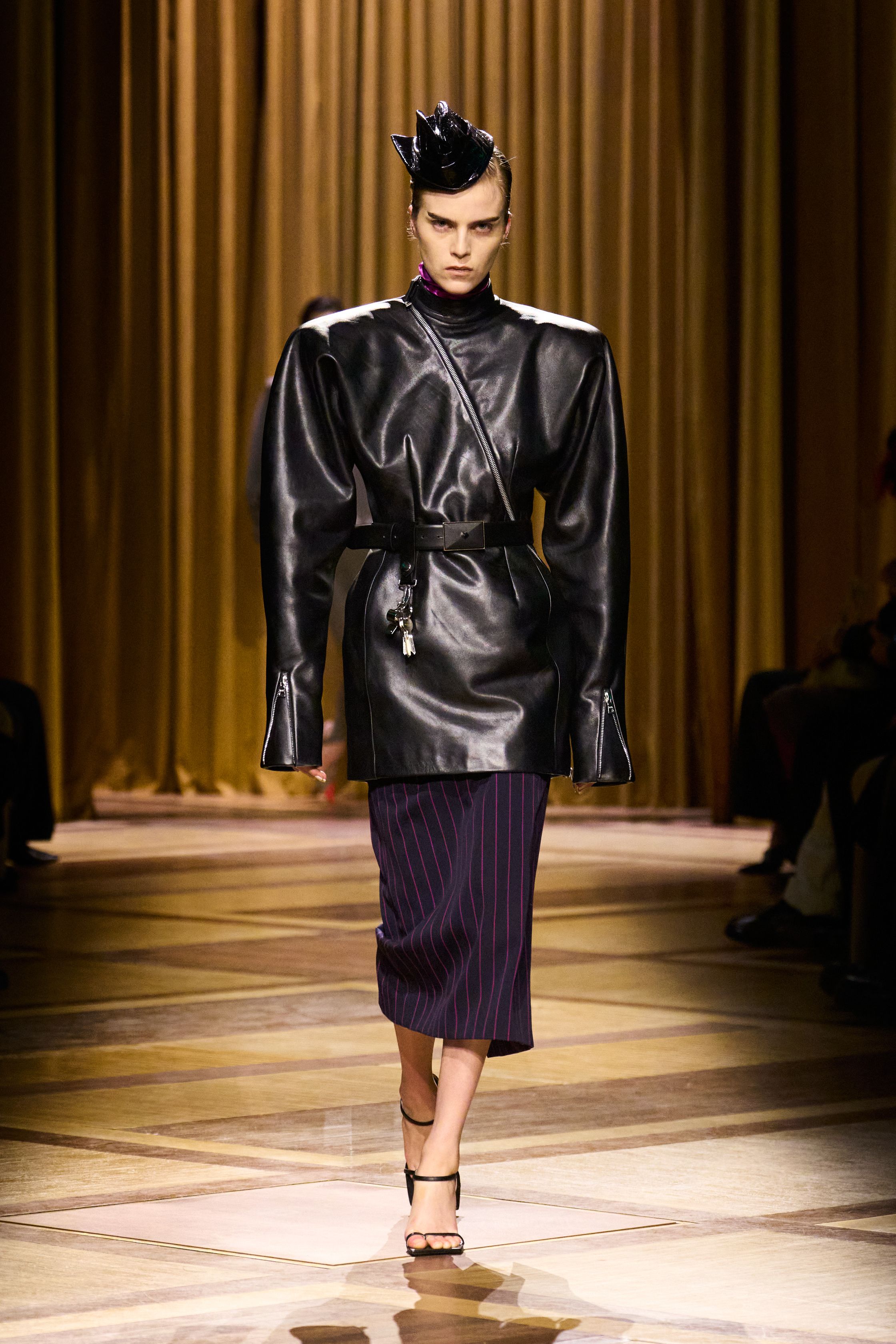 Mugler 本季继续强化品牌最核心的雕塑性感：极端肩线、收紧腰部与流畅长裤塑造出未来感女性轮廓。紫色权力套装、金属光泽衬衫和皮革裙装让整场秀既强势又华丽，仿佛科幻电影中的都市女主角-顽石频道趋势研究